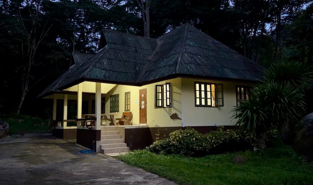 A cozy government national park bungalow cottage lit up at dusk in a forest clearing