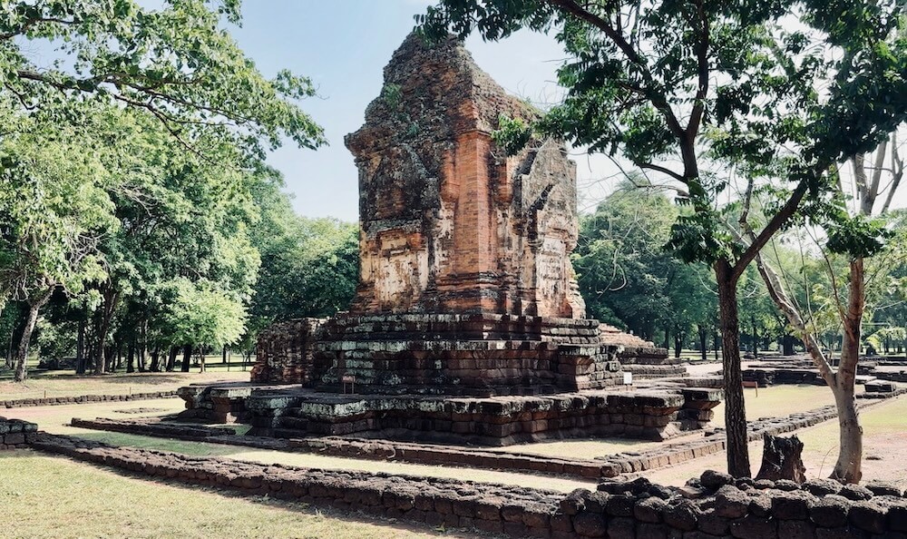 An ancient brick Khmer prang tower standing on a stepped laterite base surrounded by trees at Si Thep Historical Park.