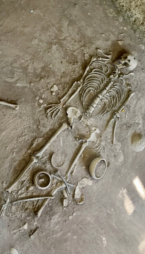 An excavated prehistoric human skeleton laid out in the earth surrounded by ancient pottery and artifacts at Si Thep Historical Park.