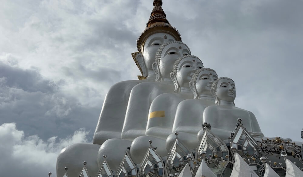 Side angle view of the five nested white Buddha statues against dramatic monsoon clouds at Wat Phra That Pha Sorn Kaew.