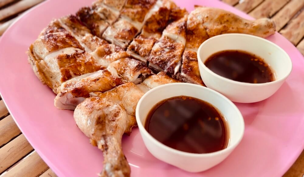 Chopped crispy Thai grilled chicken served on a pink platter with two small bowls of tamarind dipping sauce.