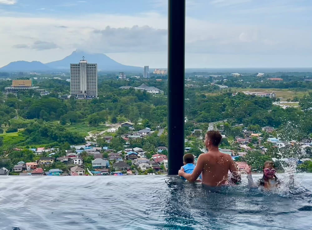 Family enjoying the rooftop infinity pool overlooking the city skyline and surrounding hills in Kuching.